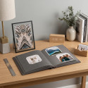 Open photo album and minimalist black photo frame with photo prints on a wooden desk